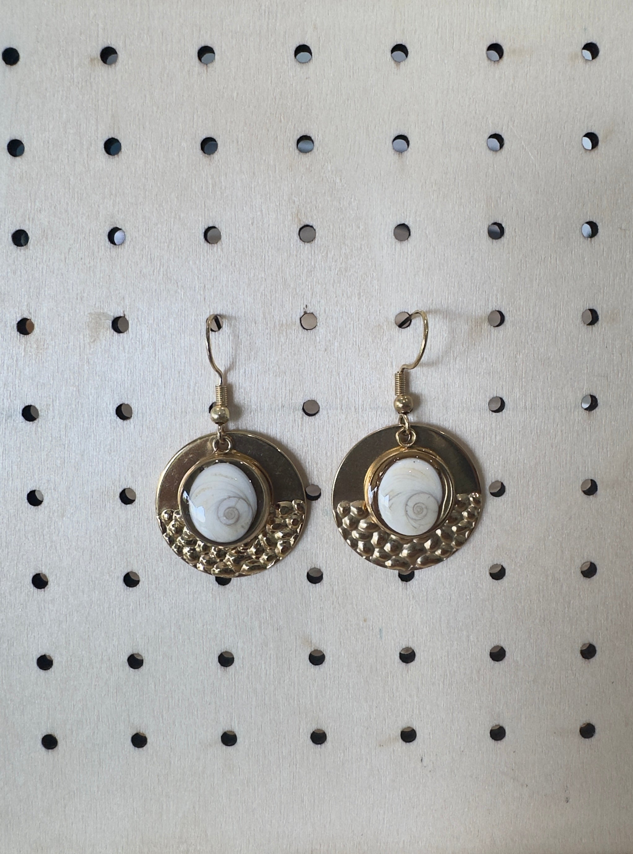 Gros plan sur le médaillon martelé doré et le cabochon Œil de Sainte-Lucie des boucles d'oreilles Nautile