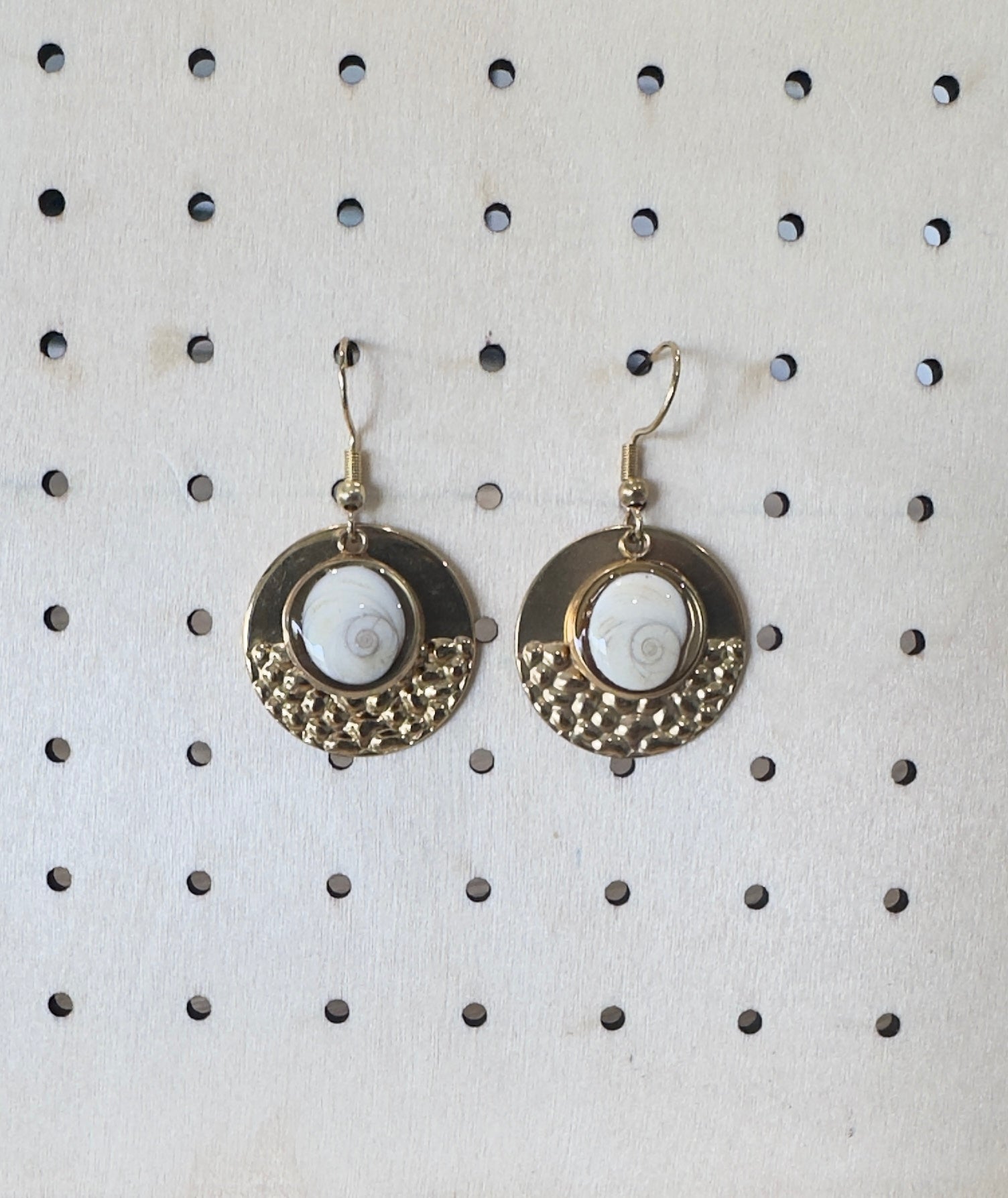 Vue rapprochée des boucles d'oreilles Nautile, médaillon doré martelé et cabochon Oeil de Sainte-Lucie