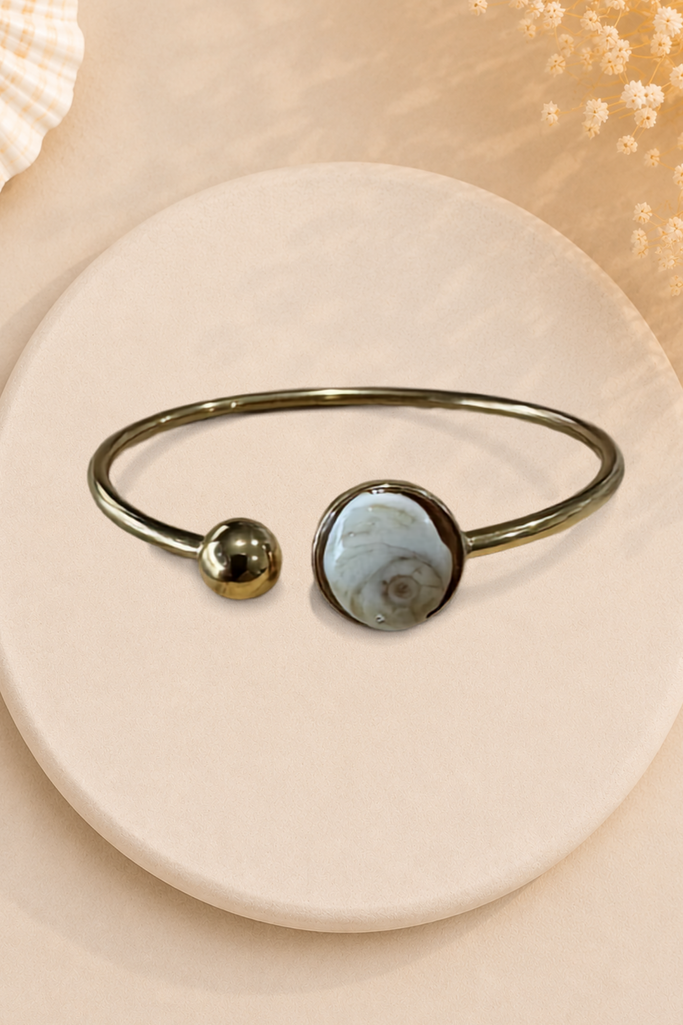 Bracelet jonc doré avec médaillon rond serti d'un Œil de Sainte-Lucie gris, style minimaliste marin.