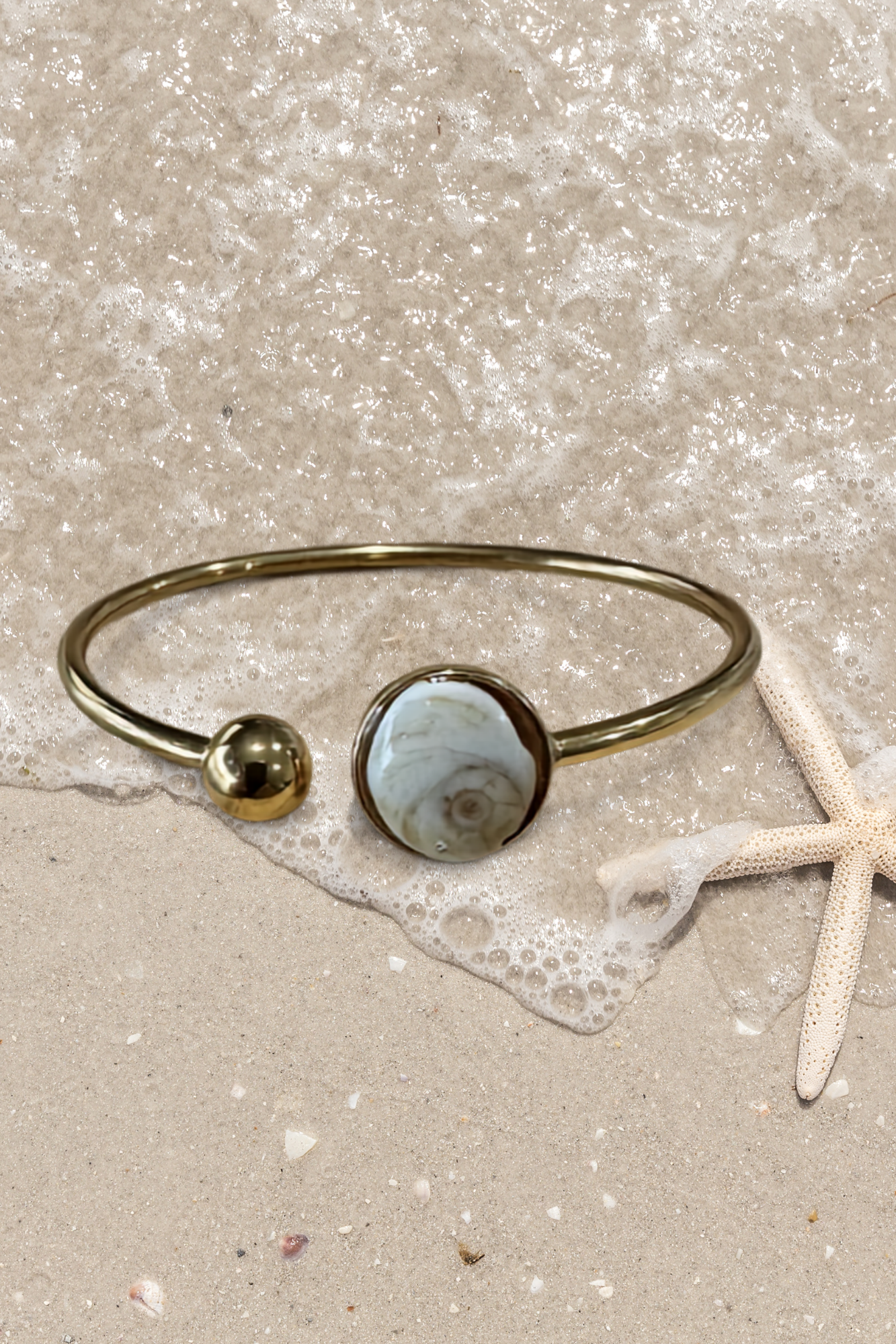 Bracelet jonc doré avec médaillon rond serti d'un Œil de Sainte-Lucie gris, style minimaliste marin.