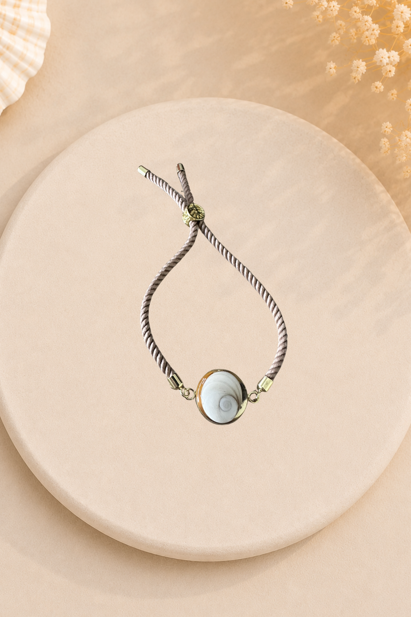 Bracelet femme Œil de Sainte‑Lucie sur cordon beige et médaillon doré. Bijou artisanal, chic et porte‑bonheur méditerranéen, élégant au quotidien.