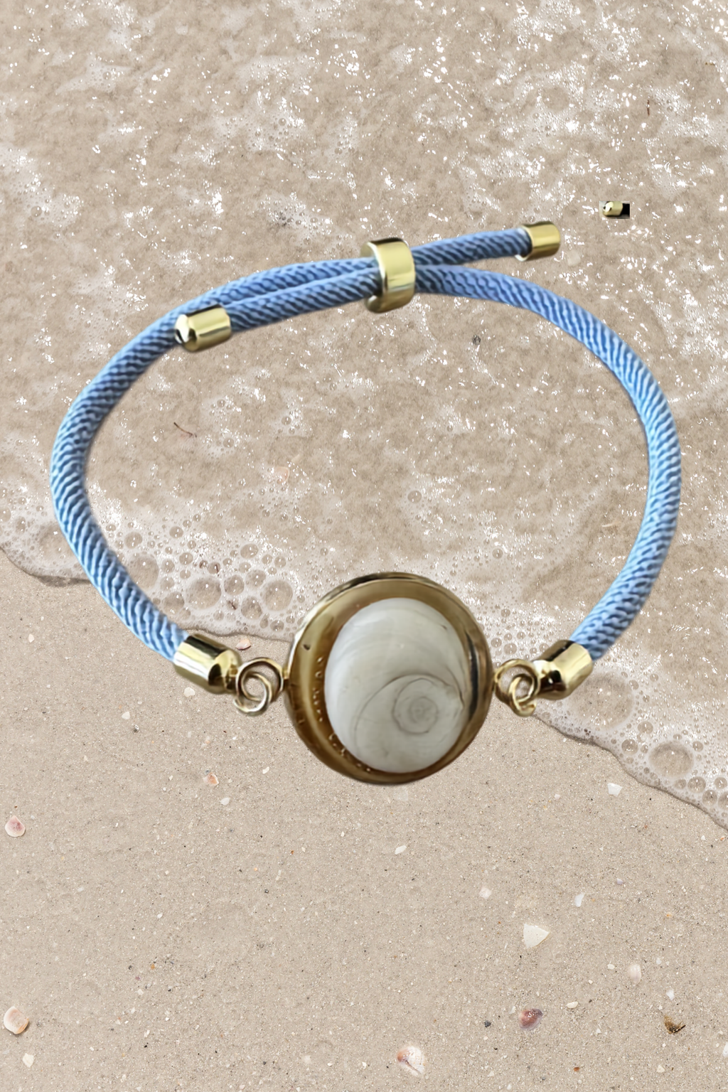 Bracelet femme, cordon bleu pâle fin, médaillon rond doré serti d’un Œil de Sainte‑Lucie blanc, style chic et minimaliste.