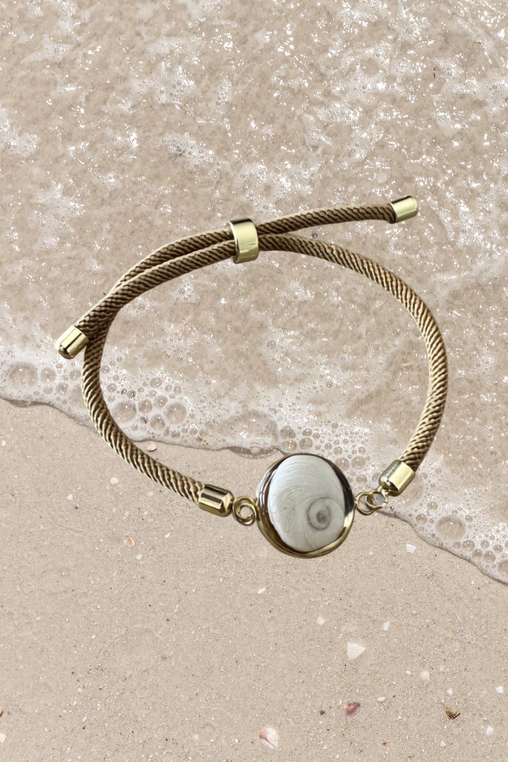 Bracelet femme, cordon marron beige fin, médaillon rond doré serti d’un Œil de Sainte‑Lucie blanc, style chic et minimaliste.