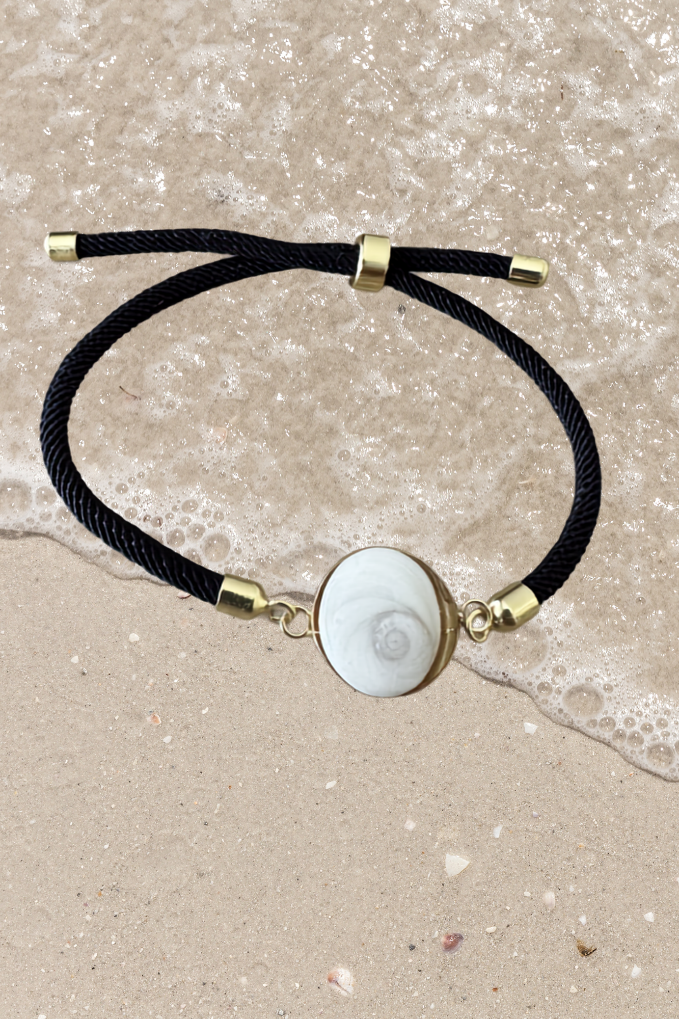 Bracelet femme, cordon noir fin, médaillon rond doré serti d’un Œil de Sainte‑Lucie blanc, style chic et minimaliste.