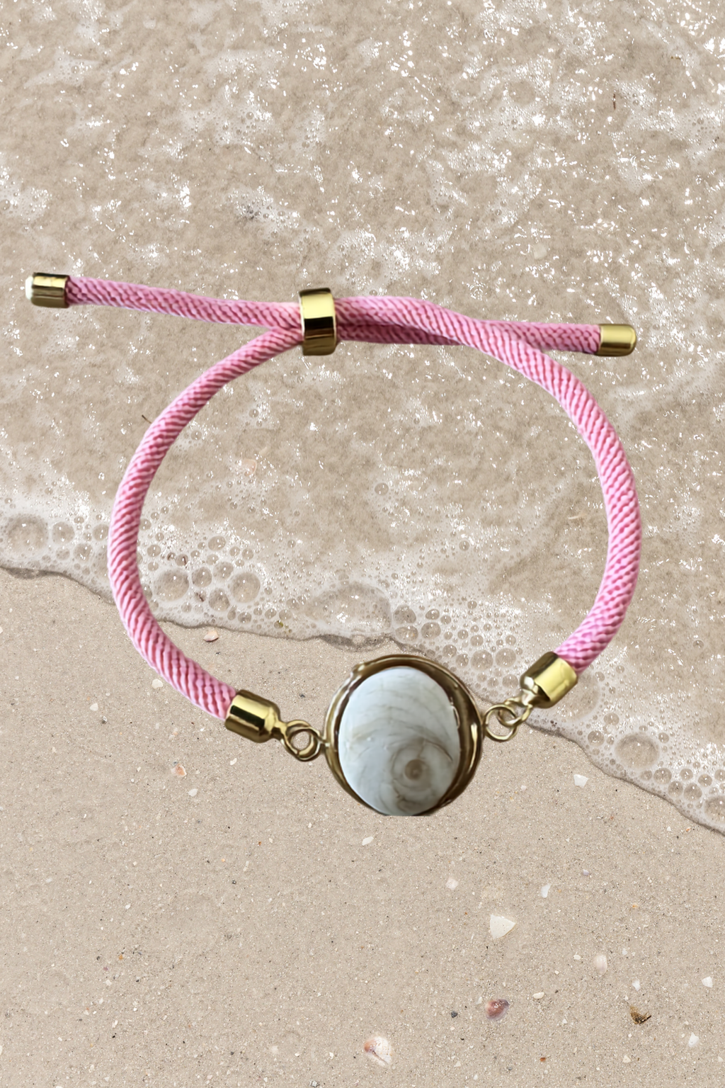 Bracelet femme, cordon rose fin, médaillon rond doré serti d’un Œil de Sainte‑Lucie blanc, style chic et minimaliste.