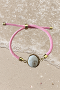 Bracelet femme, cordon rose fin, médaillon rond doré serti d’un Œil de Sainte‑Lucie blanc, style chic et minimaliste.