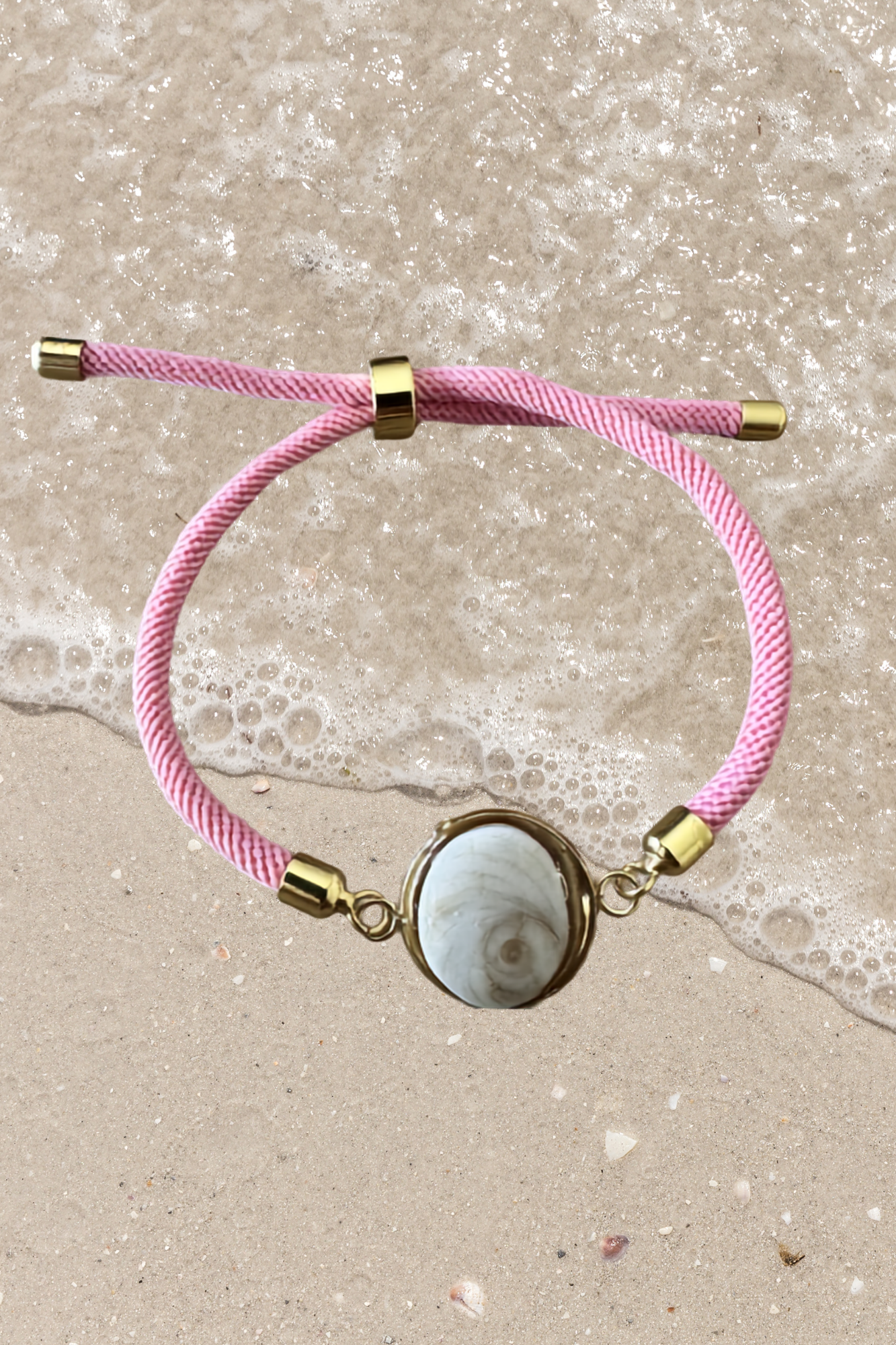 Bracelet femme, cordon rose fin, médaillon rond doré serti d’un Œil de Sainte‑Lucie blanc, style chic et minimaliste.