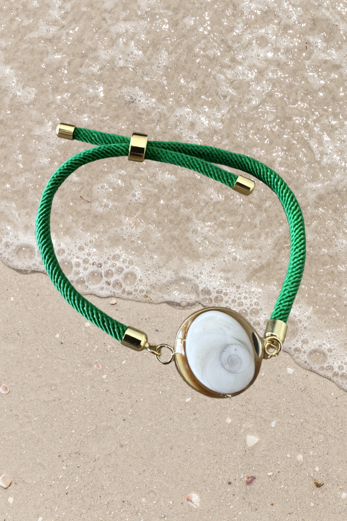 Bracelet femme, cordon vert fin, médaillon rond doré serti d’un Œil de Sainte‑Lucie blanc, style chic et minimaliste.
