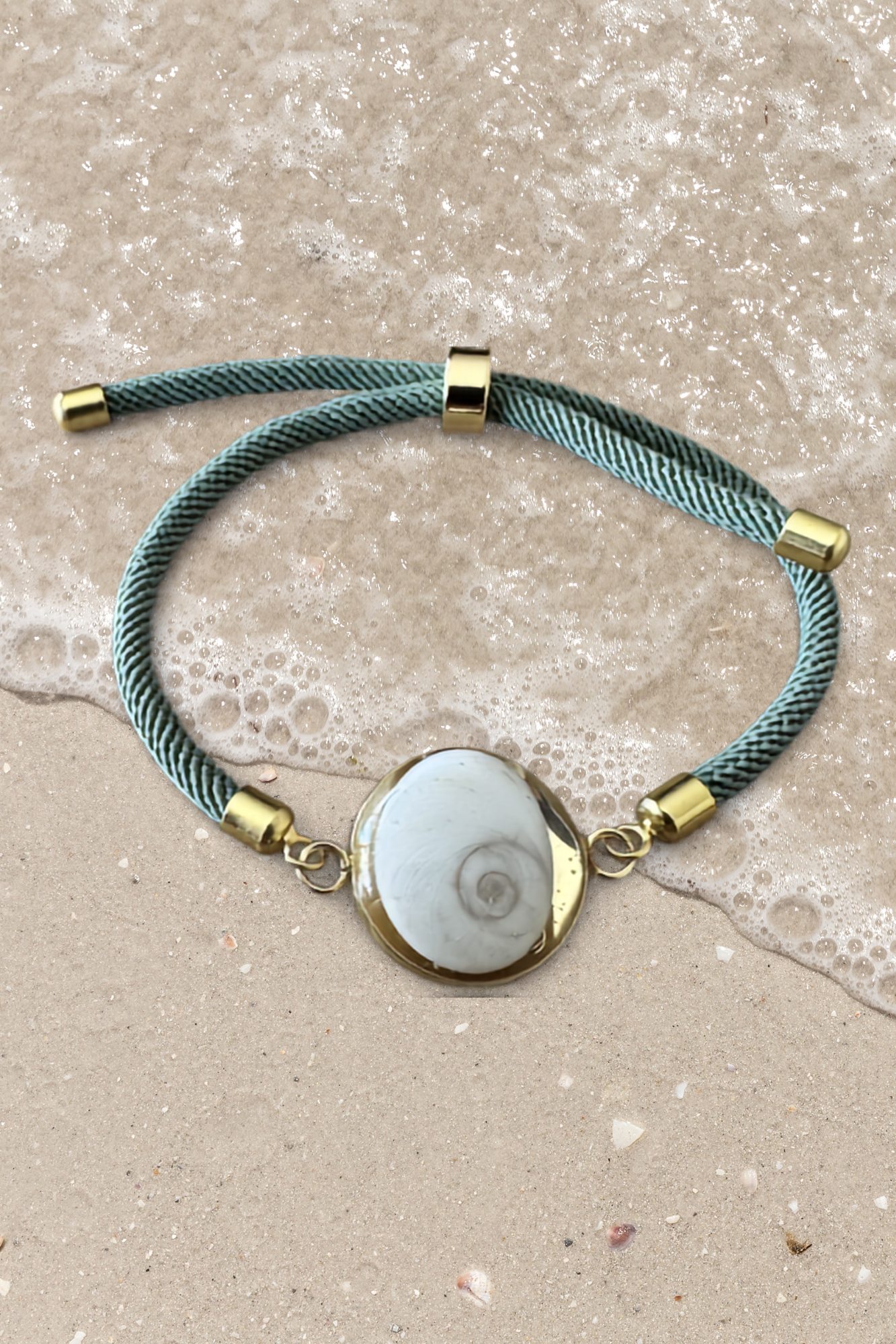 Bracelet femme, cordon vert d'eau fin, médaillon rond doré serti d’un Œil de Sainte‑Lucie blanc, style chic et minimaliste.