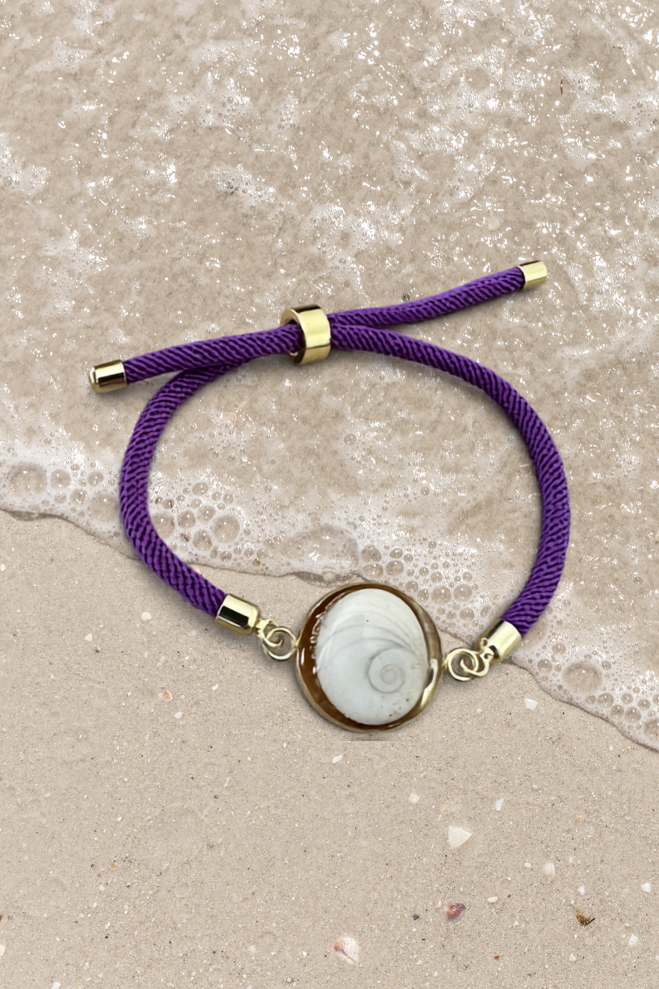Bracelet femme, cordon violet fin, médaillon rond doré serti d’un Œil de Sainte‑Lucie blanc, style chic et minimaliste.
